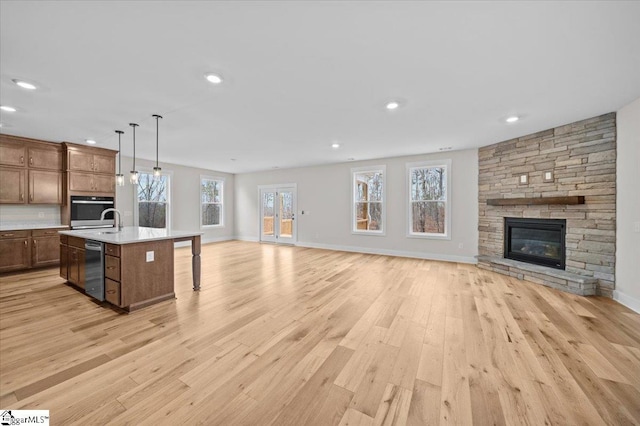 kitchen with hanging light fixtures, light hardwood / wood-style flooring, stainless steel appliances, and an island with sink