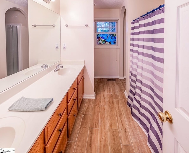 bathroom featuring wood-type flooring, vanity, walk in shower, and a textured ceiling