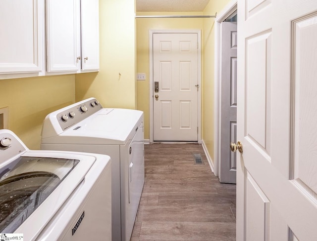 clothes washing area with washer and clothes dryer, cabinets, light wood-type flooring, and a textured ceiling