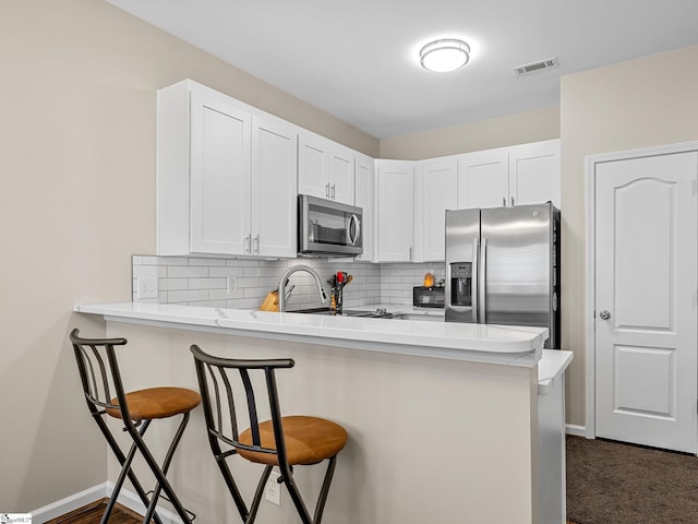 kitchen featuring appliances with stainless steel finishes, white cabinetry, tasteful backsplash, kitchen peninsula, and a kitchen bar