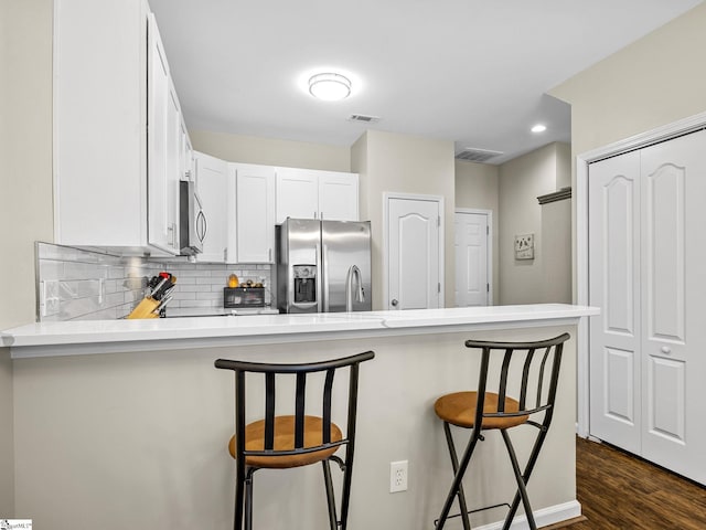 kitchen featuring kitchen peninsula, dark wood-type flooring, white cabinetry, stainless steel appliances, and a kitchen bar