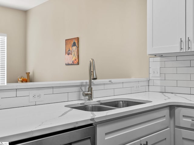 kitchen with white cabinets, light stone countertops, backsplash, and sink