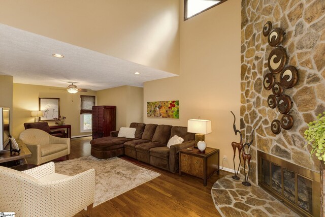 living room with a textured ceiling, hardwood / wood-style flooring, a fireplace, a towering ceiling, and ceiling fan