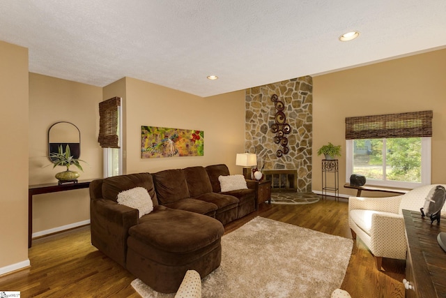 living room with a textured ceiling, a stone fireplace, and dark hardwood / wood-style floors