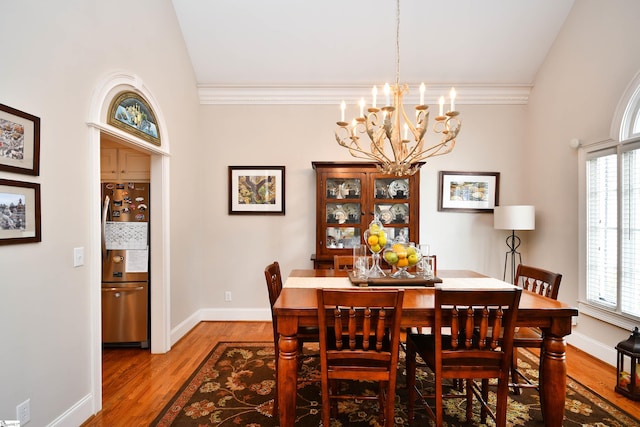 dining area with wood-type flooring, an inviting chandelier, vaulted ceiling, and a wealth of natural light