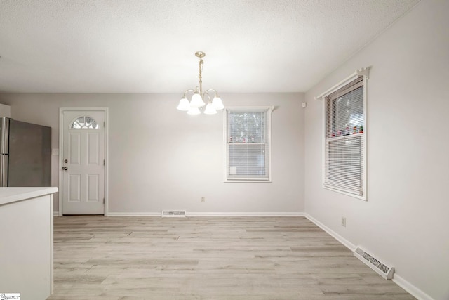 unfurnished dining area featuring a notable chandelier, light hardwood / wood-style floors, and a textured ceiling