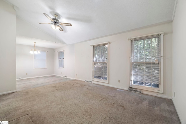 empty room featuring carpet floors, ceiling fan with notable chandelier, and vaulted ceiling