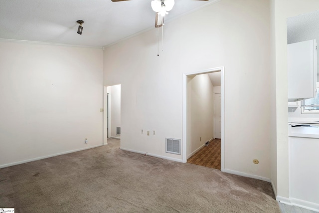 carpeted empty room featuring ceiling fan, crown molding, and a high ceiling