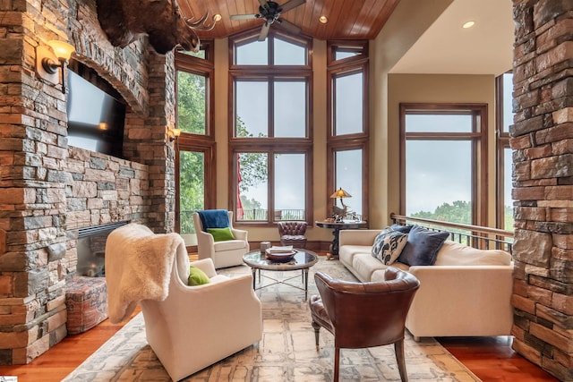 unfurnished living room with wood ceiling, light hardwood / wood-style floors, high vaulted ceiling, a stone fireplace, and ceiling fan