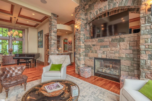 living room featuring coffered ceiling, a stone fireplace, ornate columns, hardwood / wood-style flooring, and ornamental molding