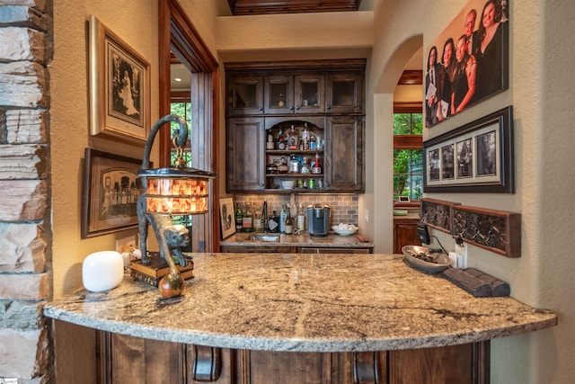 bar featuring a wealth of natural light, backsplash, dark brown cabinetry, and sink