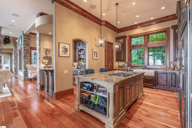 kitchen with pendant lighting, a kitchen island, light stone countertops, crown molding, and light hardwood / wood-style floors