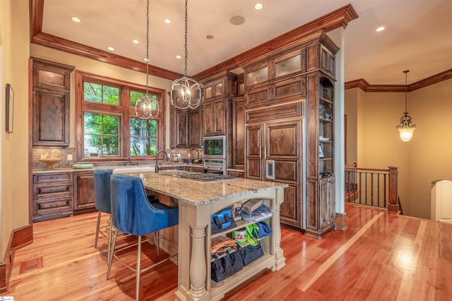 kitchen with an island with sink, decorative backsplash, light hardwood / wood-style floors, and built in appliances