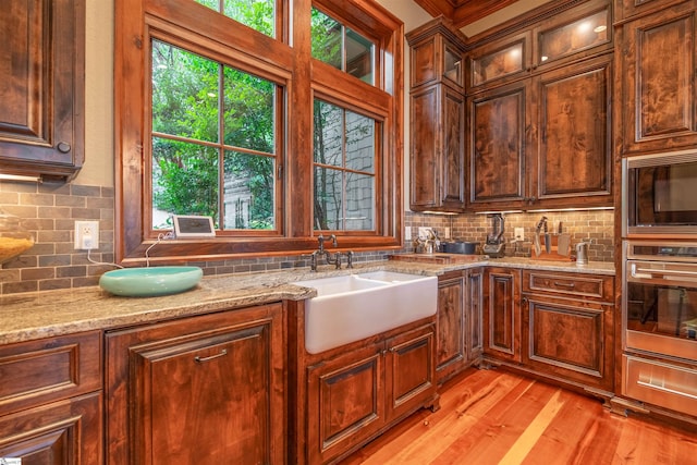 kitchen featuring light wood-type flooring, light stone counters, sink, backsplash, and appliances with stainless steel finishes