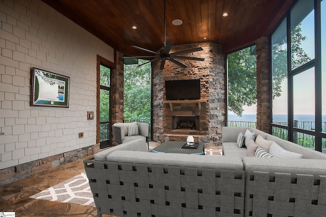 exterior space featuring an outdoor stone fireplace, ceiling fan, wooden ceiling, and a healthy amount of sunlight