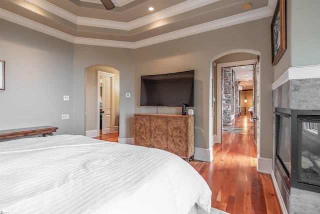 bedroom featuring ceiling fan, a raised ceiling, a multi sided fireplace, crown molding, and hardwood / wood-style floors