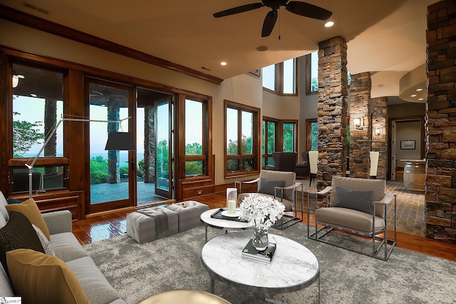 living room featuring wood-type flooring, decorative columns, ornamental molding, a high ceiling, and ceiling fan