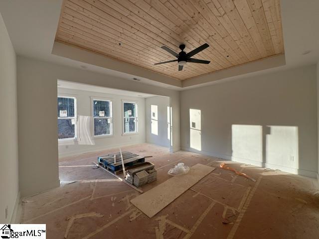 unfurnished living room featuring ceiling fan, a raised ceiling, and wood ceiling