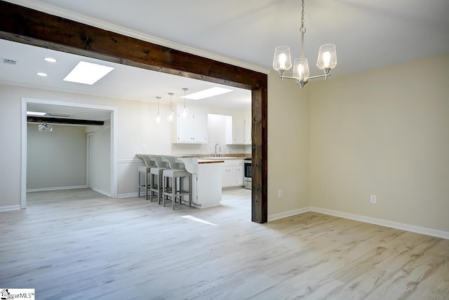 interior space featuring an inviting chandelier, light wood-type flooring, a skylight, and sink