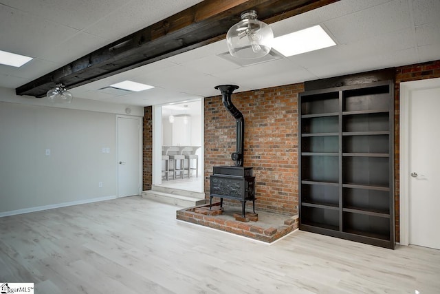 unfurnished living room featuring a wood stove, light hardwood / wood-style floors, and brick wall