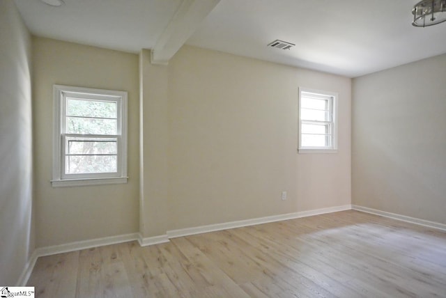 spare room with beamed ceiling, light wood-type flooring, and plenty of natural light