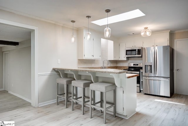 kitchen with stainless steel appliances, white cabinetry, kitchen peninsula, and a skylight