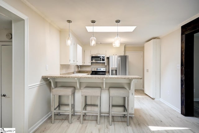 kitchen with appliances with stainless steel finishes, kitchen peninsula, light wood-type flooring, and white cabinets