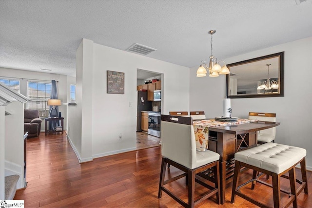 dining area with a notable chandelier, a textured ceiling, and dark hardwood / wood-style flooring