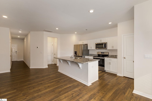 kitchen with an island with sink, stainless steel appliances, white cabinets, and dark hardwood / wood-style flooring