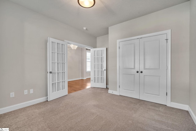 unfurnished bedroom featuring a closet, light colored carpet, french doors, and a textured ceiling