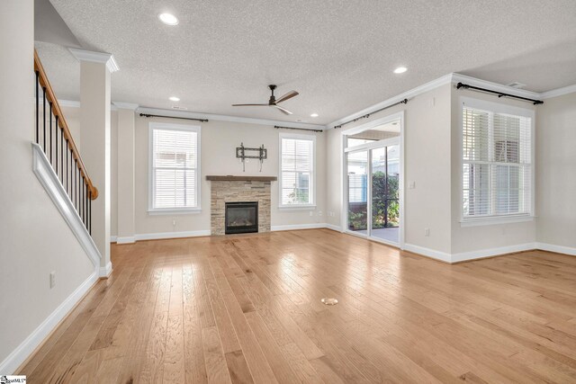 unfurnished living room with ceiling fan, a textured ceiling, a fireplace, light wood-type flooring, and crown molding