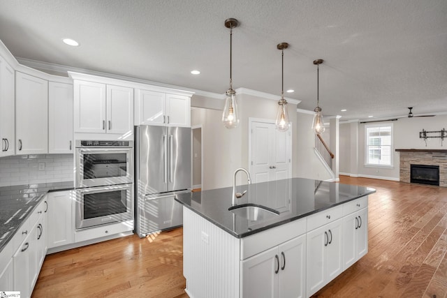 kitchen with hanging light fixtures, white cabinets, stainless steel appliances, light hardwood / wood-style flooring, and sink