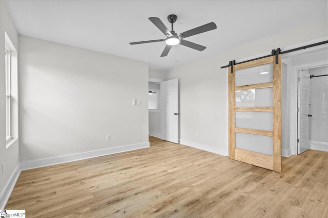 unfurnished bedroom featuring ceiling fan, light wood-type flooring, and a barn door