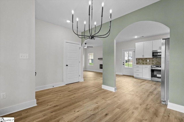 kitchen featuring light hardwood / wood-style floors, ceiling fan with notable chandelier, white cabinetry, decorative backsplash, and stainless steel appliances