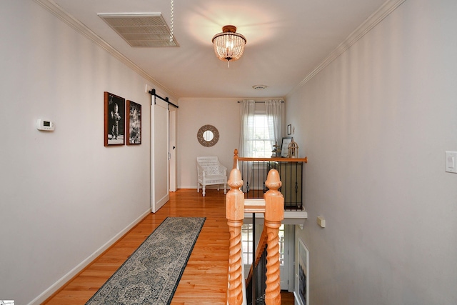 corridor featuring a barn door, ornamental molding, hardwood / wood-style floors, and a chandelier