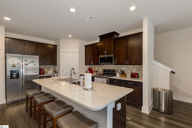 kitchen featuring appliances with stainless steel finishes, decorative backsplash, a center island with sink, dark hardwood / wood-style floors, and sink