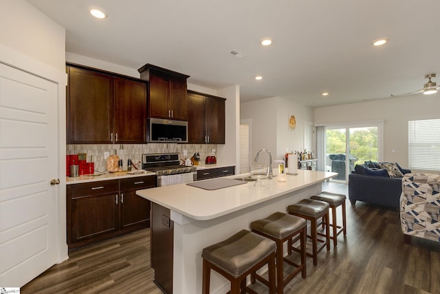 kitchen with appliances with stainless steel finishes, a center island with sink, a breakfast bar area, and dark hardwood / wood-style flooring