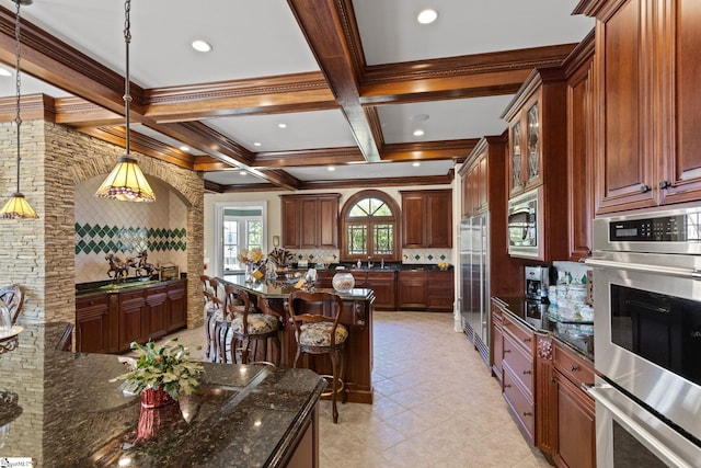 kitchen with pendant lighting, coffered ceiling, stainless steel appliances, dark stone counters, and a kitchen bar