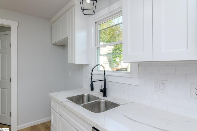 kitchen featuring light stone counters, white cabinets, sink, light wood-type flooring, and decorative backsplash