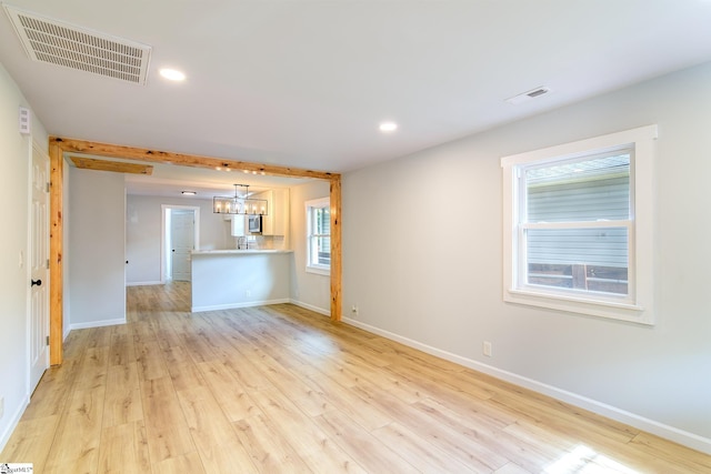 unfurnished living room featuring a notable chandelier and light hardwood / wood-style floors