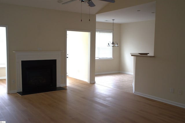 unfurnished living room featuring vaulted ceiling, ceiling fan with notable chandelier, and hardwood / wood-style floors