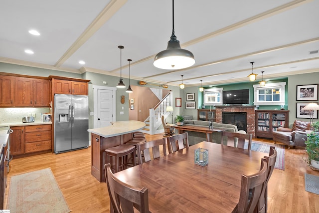 dining room with beamed ceiling, crown molding, a brick fireplace, and light hardwood / wood-style flooring