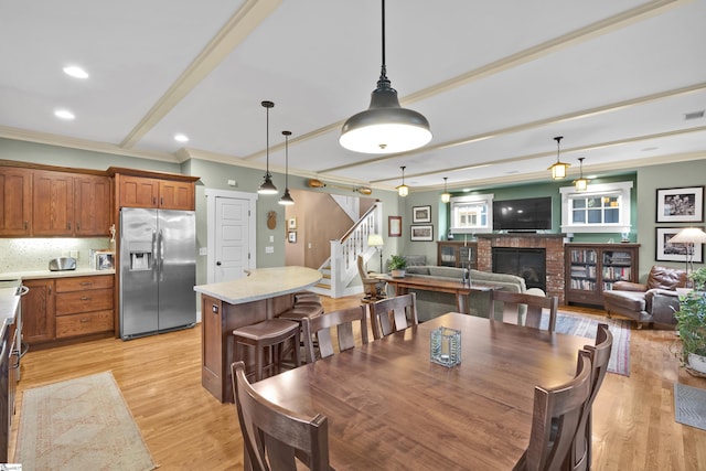 dining area with a brick fireplace, light hardwood / wood-style flooring, and ornamental molding