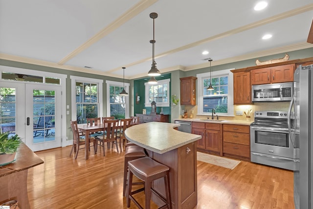 kitchen with appliances with stainless steel finishes, sink, hanging light fixtures, a center island, and light wood-type flooring