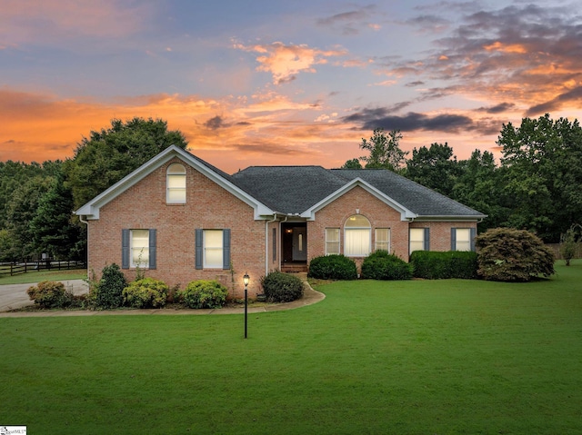 view of front of home featuring fence, a yard, and brick siding