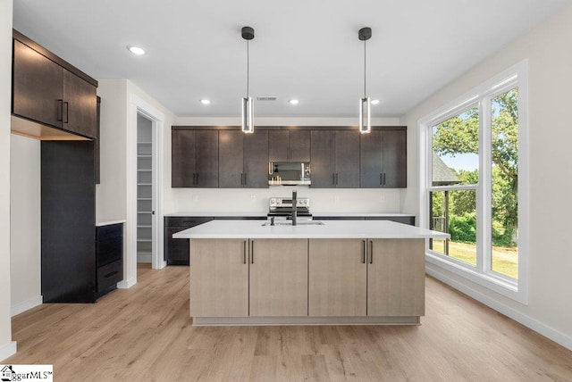 kitchen featuring an island with sink, plenty of natural light, stainless steel appliances, and decorative light fixtures