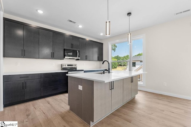 kitchen with pendant lighting, sink, a kitchen island with sink, light hardwood / wood-style flooring, and appliances with stainless steel finishes