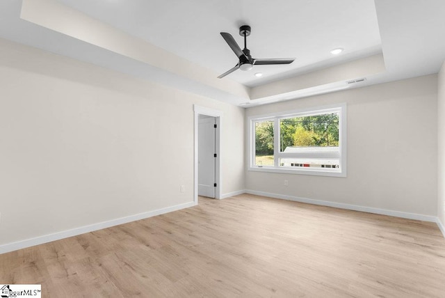 spare room with a raised ceiling, light hardwood / wood-style floors, and ceiling fan