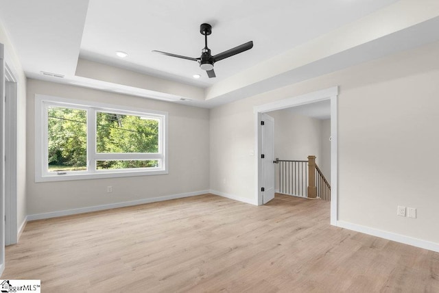 spare room with ceiling fan, light hardwood / wood-style flooring, and a tray ceiling