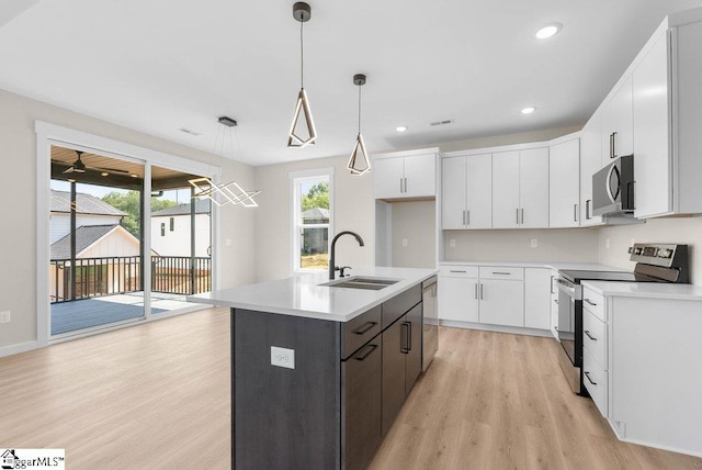 kitchen featuring hanging light fixtures, an island with sink, white cabinets, stainless steel appliances, and sink